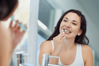 Woman brushing her teeth whilst looking in the mirror