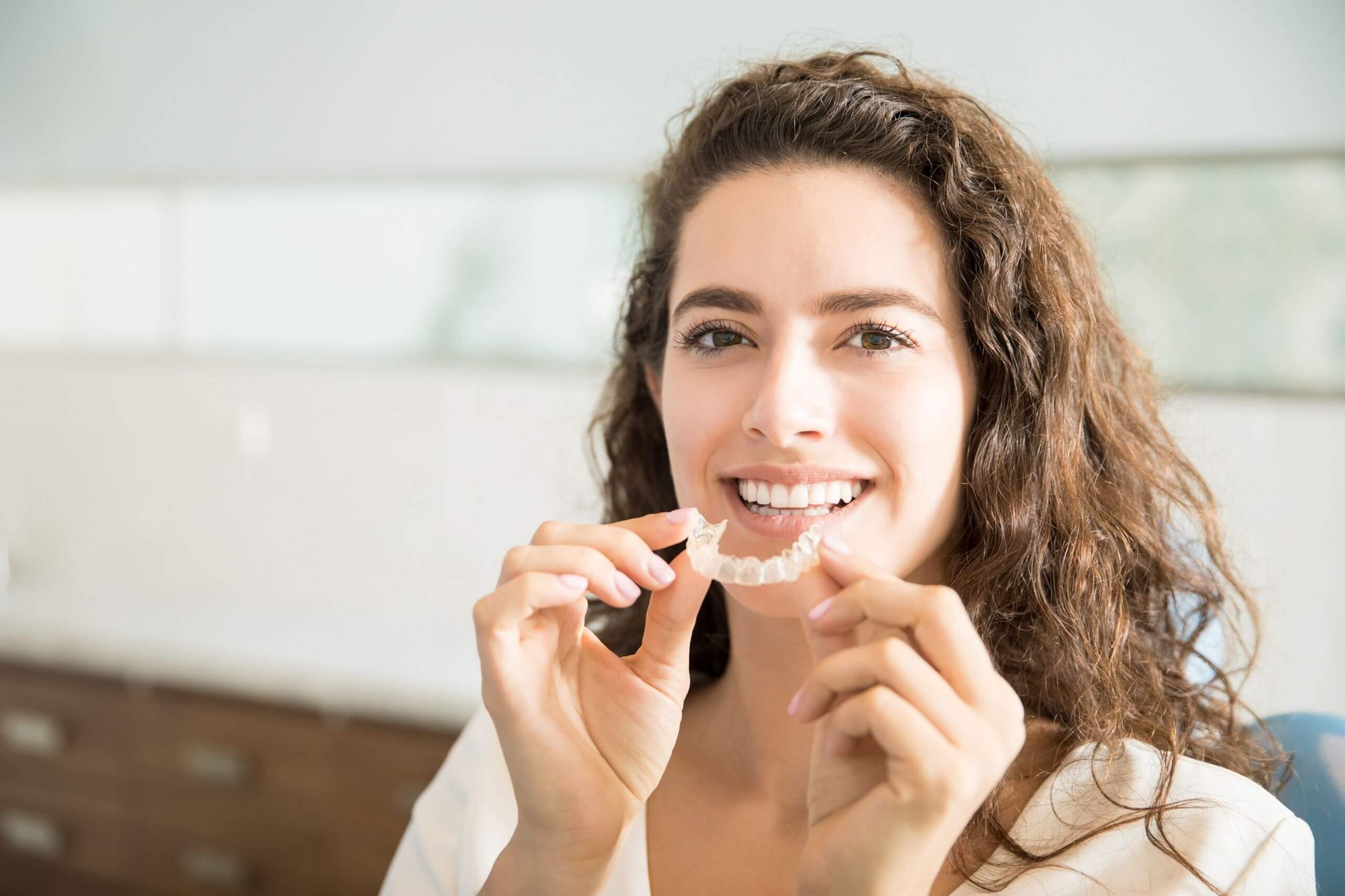 A woman holding Invisalign braces and smiling, Harwood Dental Care