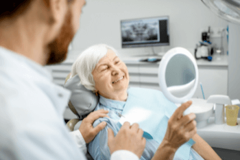 An older woman looking in the mirror at her dental implants