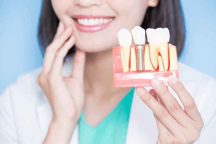 woman with straight teeth smiling and holding dental implants